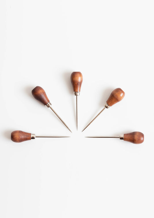 Flatlay of five awls arranged in a circle, all with wood handles and metal points.