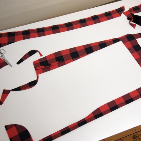 Red and black buffalo plaid coat lining pieces cut and laid out on a white cutting mat with small scissors