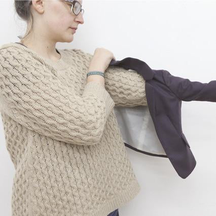 Person in a cream textured knit sweater holding up a purple mini-blazer to show the bagged lining construction