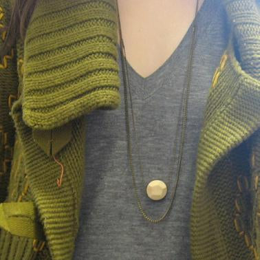 Layered necklace with light wood pendant worn over gray v-neck tee and chartreuse ribbed cardigan with striped sleeves