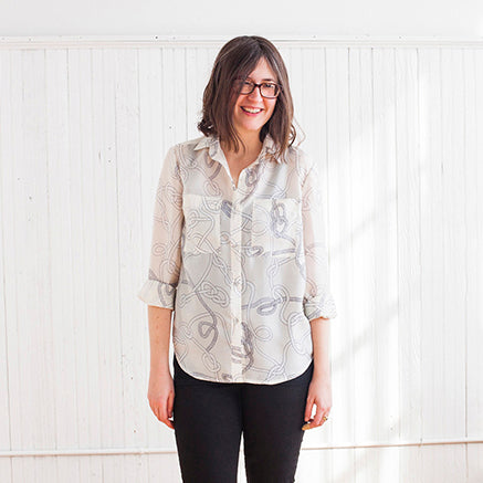 Smiling woman wearing an Archer Button-Up in ivory rope print silk habotai with rolled sleeves, paired with black pants
