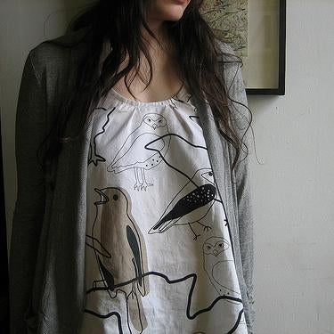 Sleeveless white tank with gathered scoop neck and black line-drawn bird print, worn under a gray cardigan