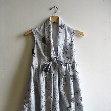 Sleeveless tie-front dress in gray leaf and acorn print fabric, hung on wooden hanger against white wall