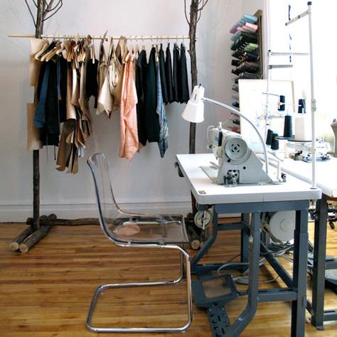Sewing studio with branch clothing rack, industrial sewing machine, acrylic chair, and thread storage on wood floors