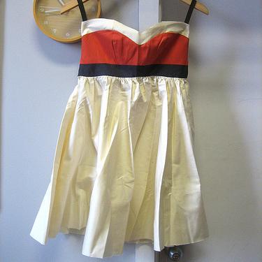 Sleeveless dress with coral, cream, and gray color-blocked bodice and gathered cream skirt on hanger