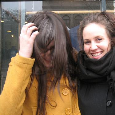 Two people outdoors, one in a mustard yellow coat with button details and one in a black scarf and jacket