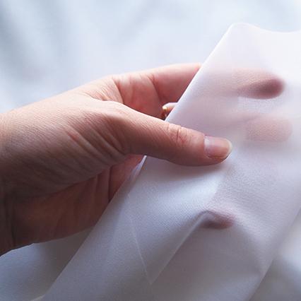 Hand holding white lightweight woven fusible interfacing, showing its semi-sheer drape and weight