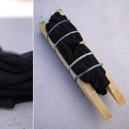 Black fabric bundled with rubber bands and wooden dowels, prepared for bleach tie-dye technique