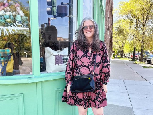 Jen Beeman in pink floral Poppy Dress with black crossbody bag, standing outside mint green storefront in spring
