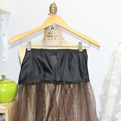 Vintage dress underskirt on wooden hanger with black lining and layered neutral tulle skirt during alteration project