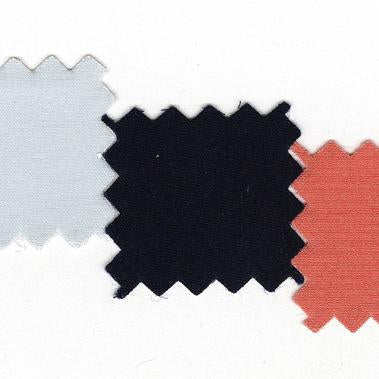 Three fabric swatches with pinked edges in light blue, navy, and coral laid flat for color coordination planning