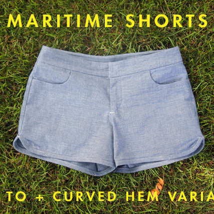 Maritime Shorts in light blue chambray with curved hem variation displayed on grass with yellow text overlay