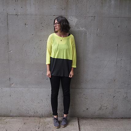 Person in a neon yellow and charcoal colorblock Hemlock Tee with three-quarter sleeves and black jeans against concrete wall