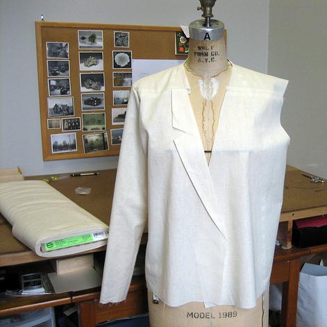 White blazer muslin with notch lapels on dress form in a sewing studio with reference board and ironing board in background