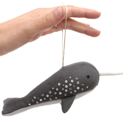 Hand holding a gray felt narwhal ornament with silver sequin details and a string loop for hanging