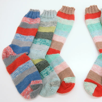 Hand-knit striped socks in colorful combinations including blue, pink, gray, yellow, red, and mint on a white background