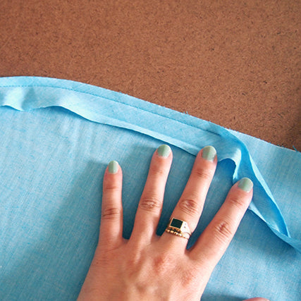 Hand pressing a folded bias binding strip along the edge of light blue chambray fabric for the Lakeside Pajamas shorts