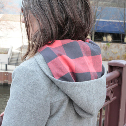 Woman wearing Cascade Duffle Coat with gray body and red charcoal plaid contrast yoke and hood, shown from back view outdoors