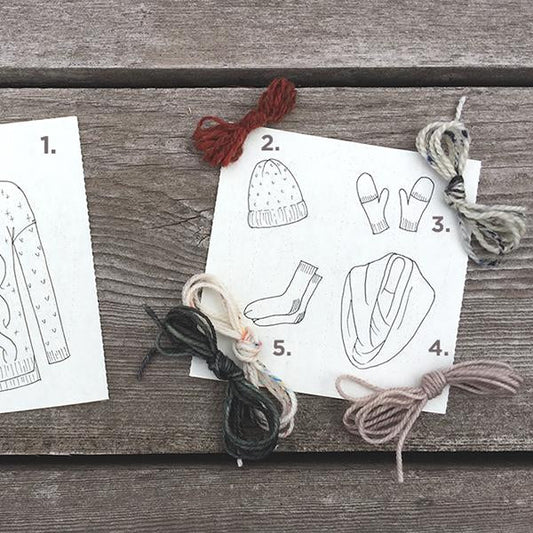 Sewing pattern sketches numbered 1-5 showing outerwear and accessories designs, displayed on gray wood with colored yarn bundles