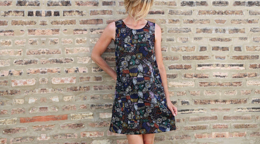 Willow Dress in navy multicolor daisy print, sleeveless A-line silhouette with crew neckline, standing against brick wall