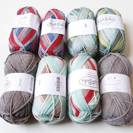 Eight Knit Picks yarn balls in colorways including red and blue striped, gray, and multicolor with white paper labels