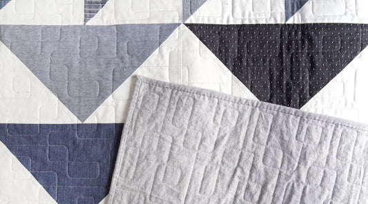 Four Winds quilt close-up showing triangle blocks in white, gray stripe, black dot, and navy with visible quilting stitches