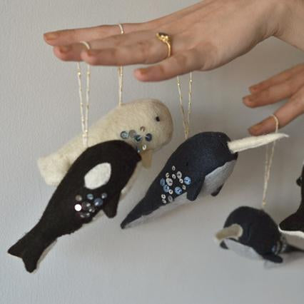 Hand holding handmade felt whale ornaments in cream, navy, and black with sequin and embroidered details on gold string