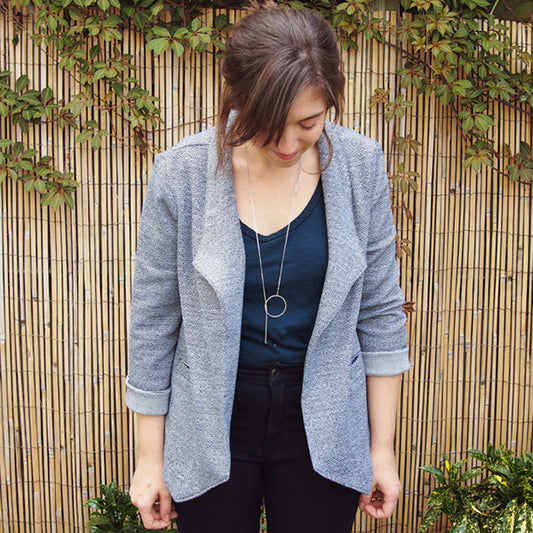 Woman wearing gray heathered knit Morris Blazer over navy tank and black pants, standing against wooden slat and ivy backdrop
