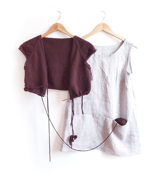 Finished gray linen Uniform Tunic beside in-progress deep purple Uniform Sweater in wool yarn, both on wooden hangers