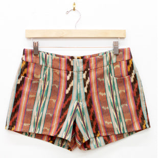 Maritime Shorts in rust, green, and cream ikat cotton with fly front and curved front pockets on a wooden hanger