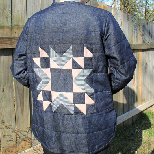 Back view of indigo denim Tamarack Jacket with cream and blue quilted star block appliqué, worn outdoors against a wood fence