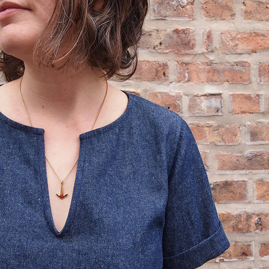 Close-up of Scout Tee variation in indigo denim showing notched neckline, short cuffed sleeves, and a gold anchor necklace