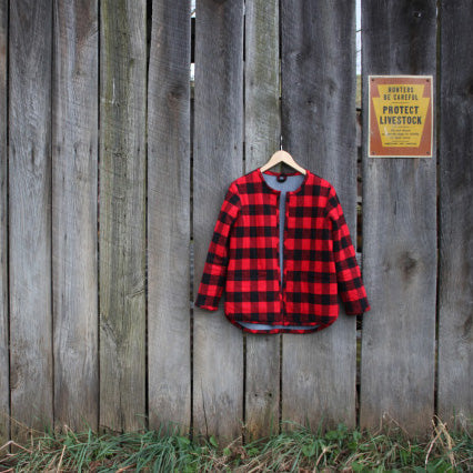 Tamarack Jacket in red and black buffalo check with chambray lining, hanging on wooden wall with vintage sign