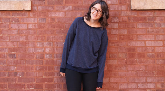 Linden Sweatshirt View A in navy French terry with ribbed neckline and cuffs, worn with black pants against red brick wall