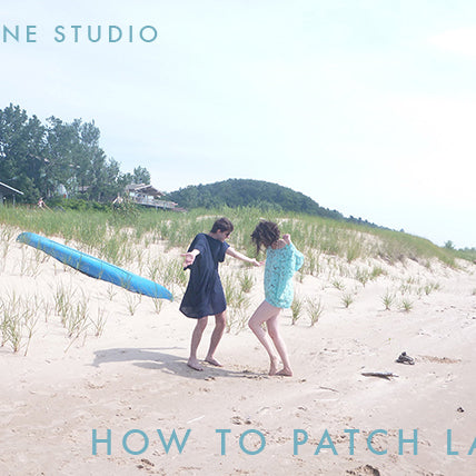 Grainline Studio video thumbnail of two people on a sandy beach with a blue paddleboard and dune grass in the background