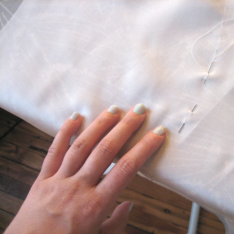 Hand with manicured nails resting on ivory silk lining fabric with hand-sewn basting stitches visible