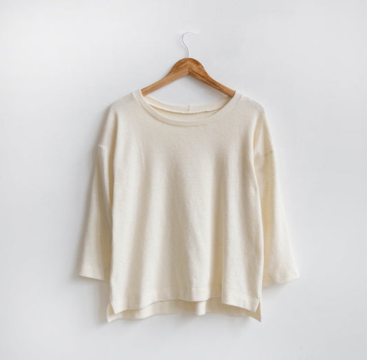 Hemlock Tee in cream wool knit with three-quarter sleeves and split side hem, displayed on wooden hanger