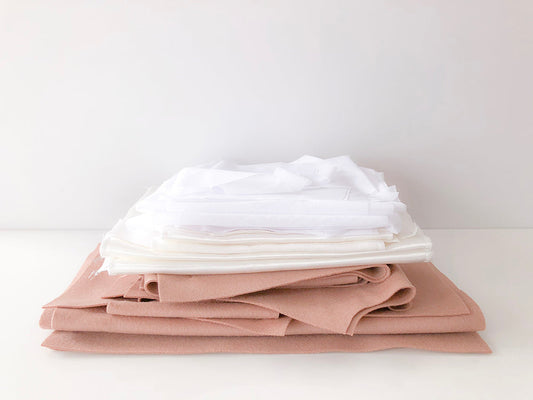 Stack of folded Yates Coat fabric: white fusible interfacing, Kashi lining, and blush wool coating