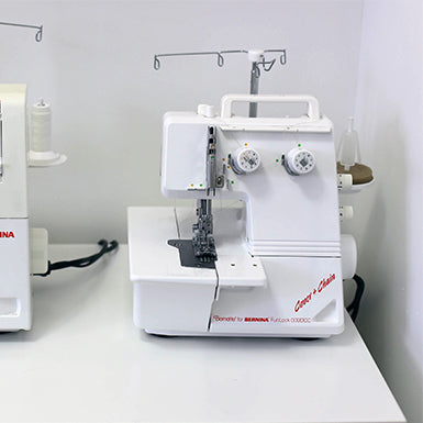 White BERNINA serger and coverstitch machines on IKEA MICKE desk with cord hole in front corner for scrap management