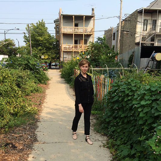 Person wearing black silk Archer Button Up Shirt sleeveless version in an urban garden with row houses in background