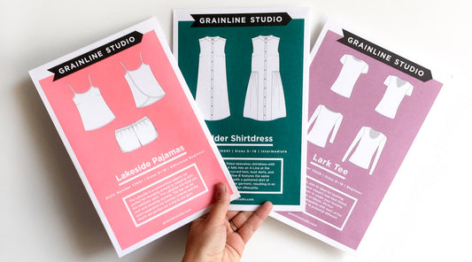 Three Grainline Studio pattern envelopes: Lakeside Pajamas in coral, Alder Shirtdress in teal, and Lark Tee in mauve