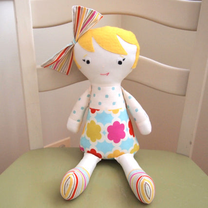 Handmade fabric doll with yellow hair, striped bow, colorful floral dress, and striped socks on a green chair