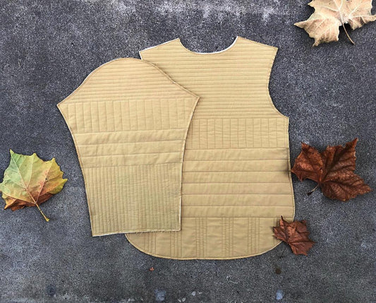 Tamarack Jacket front and back pieces in muted yellow with grid channel quilting, laid flat with autumn leaves