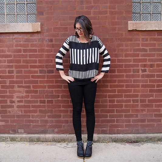 Hemlock Tee in black and white striped silk with color-blocked stripe placement, worn with black jeans against brick wall