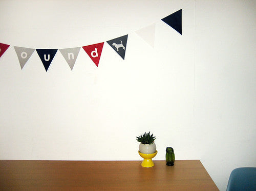 Bunting banner spelling "hound" in burgundy, gray, cream, and navy flags above a wooden desk with a small succulent