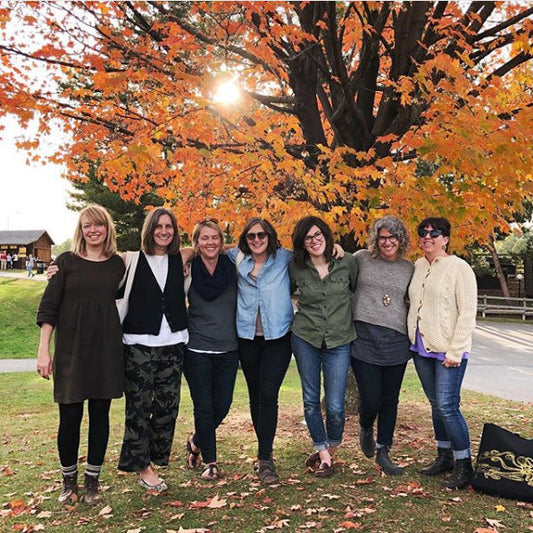 Group of seven women standing together under a large tree with golden fall foliage, at the New York Sheep & Wool Festival