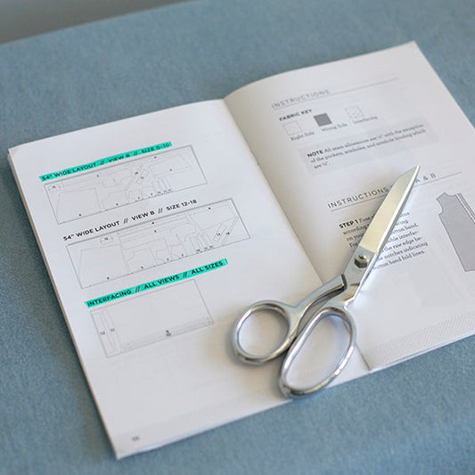 Alder Shirtdress pattern booklet open to cutting layouts and instructions, with teal highlights and silver dressmaking scissors