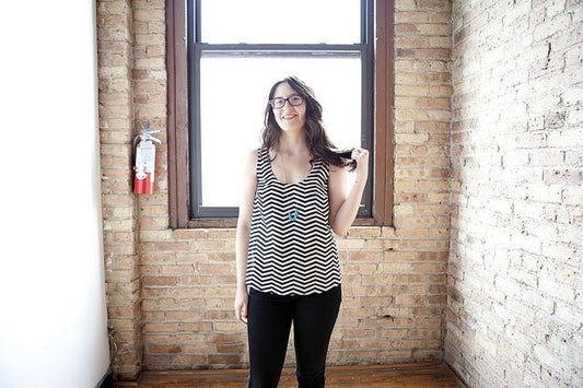 Woman wearing black and white chevron Tiny Pocket Tank with black pants standing in front of a brick wall window