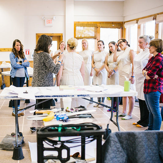 Instructor demonstrating sloper fitting at Camp Workroom Social, with participants in muslin test garments around a worktable