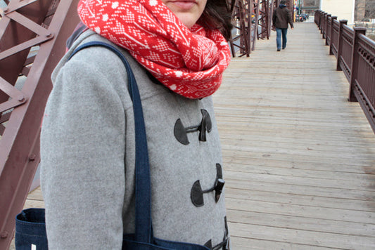 Woman in a gray wool duffle coat with toggle closures and a red Fair Isle infinity scarf on a wooden bridge